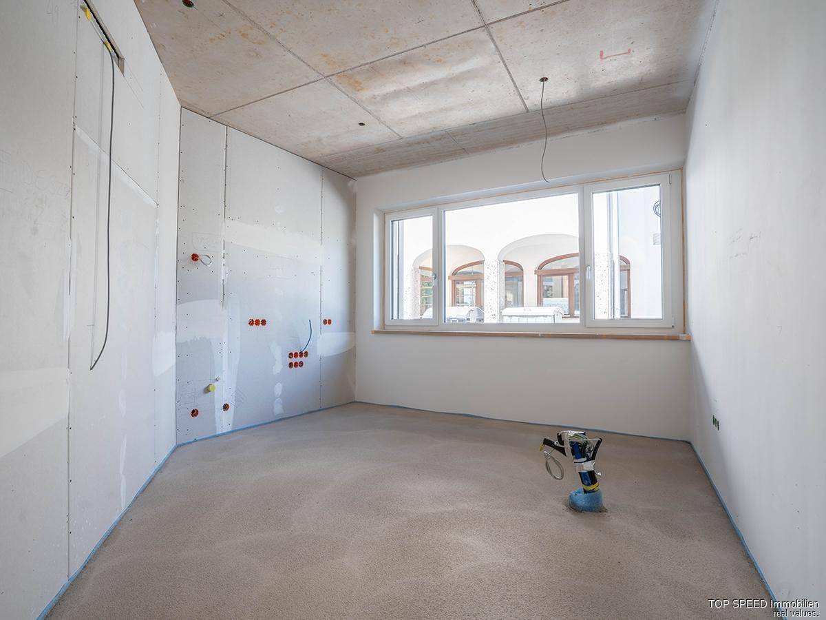 Unfertiger Raum mit großem Fenster und Blick auf die Umgebung, bereit für den Innenausbau.