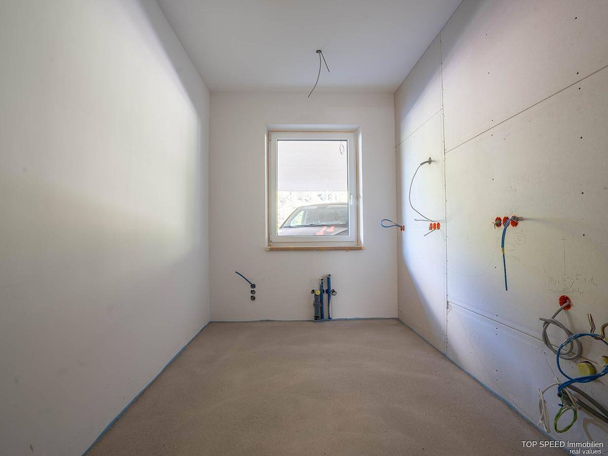 Kleiner Rohbau-Raum mit Fenster und sichtbaren Sanitäranschlüssen für ein zukünftiges Bad oder WC.