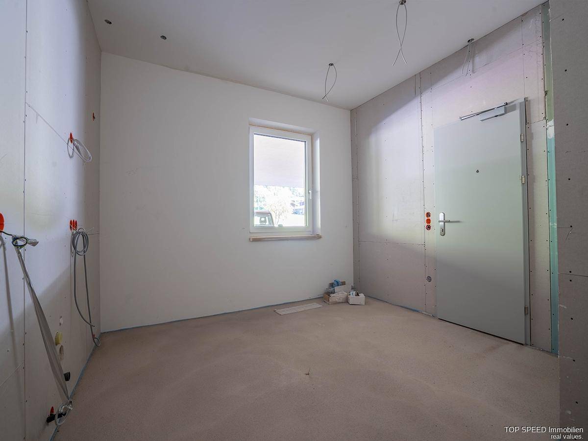 Rohbau-Raum mit Fenster und Eingangstür, bereit für die individuelle Gestaltung und Nutzung.