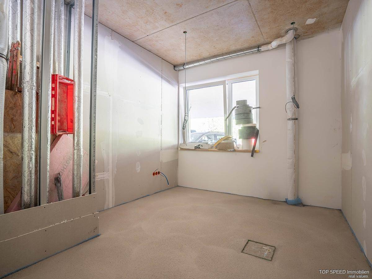 Unfertiger Raum mit Fenster und sichtbaren Rohren, ideal für einen Technik- oder Abstellraum.