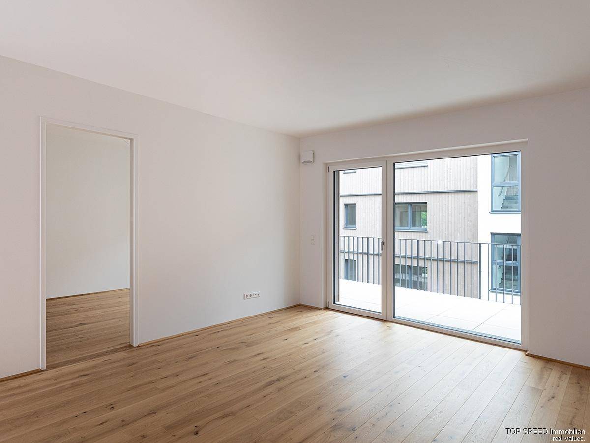 Lichtdurchfluteter Wohnraum mit modernem Parkettboden und direktem Zugang zum Balkon.