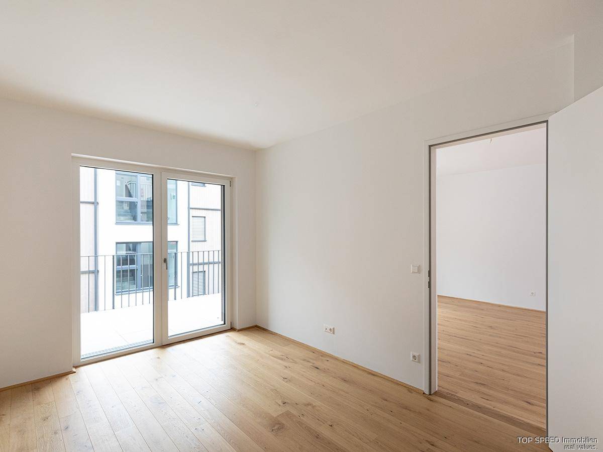 Neuwertiger Wohnbereich mit hellen Wänden, Holzboden und großem Balkonzugang, ideal für modernes Wohnen.