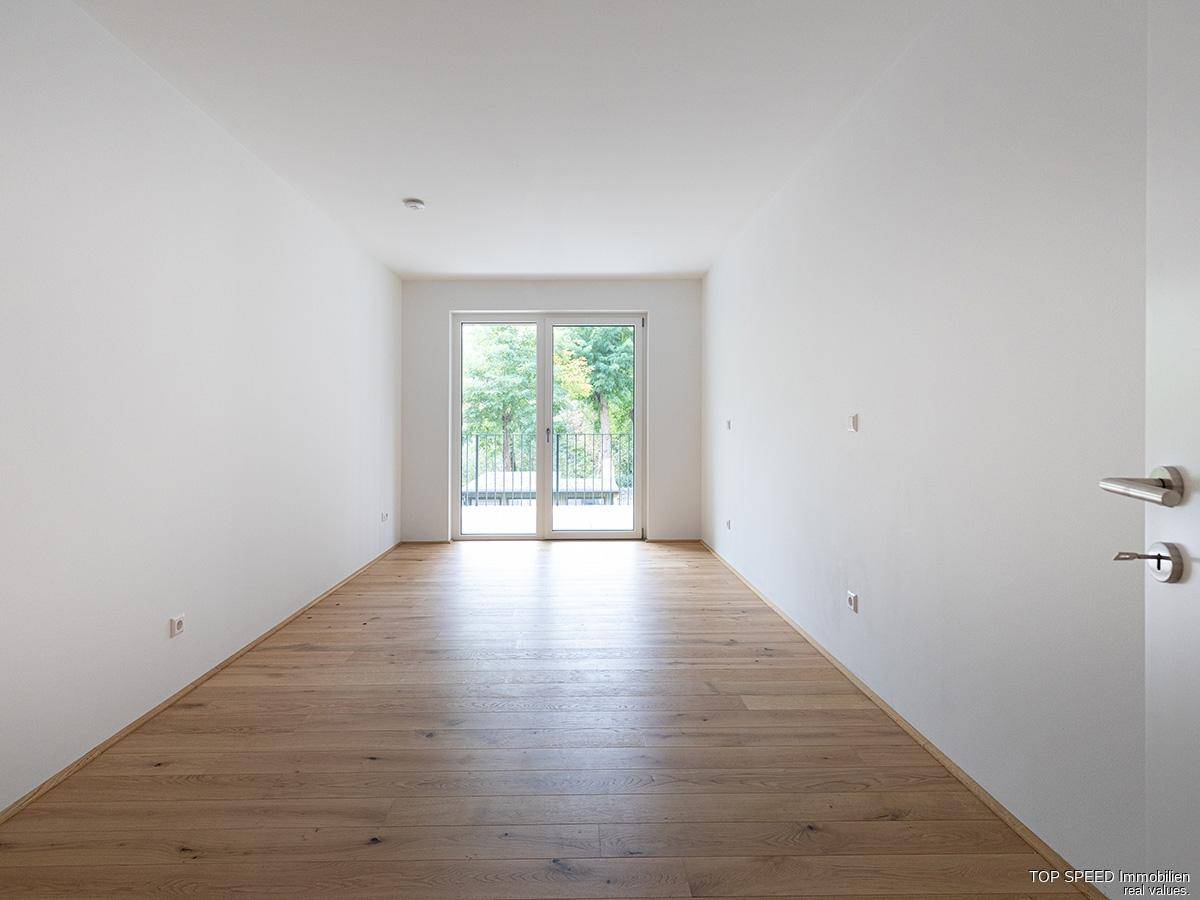 Leeres Zimmer mit hellem Parkettboden und Zugang zu einem französischen Balkon.