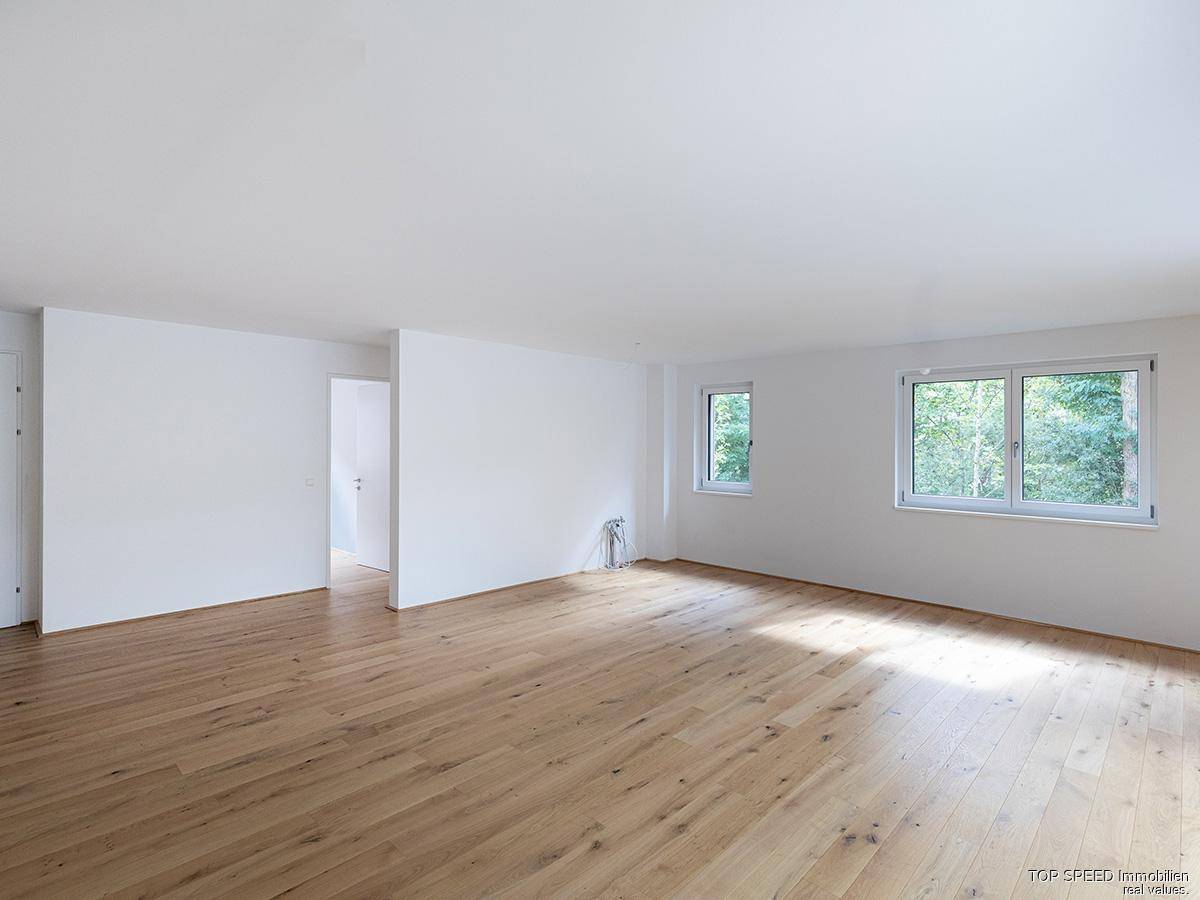 Heller Wohnraum mit Parkettboden und mehreren Fenstern, die viel Tageslicht hereinlassen.