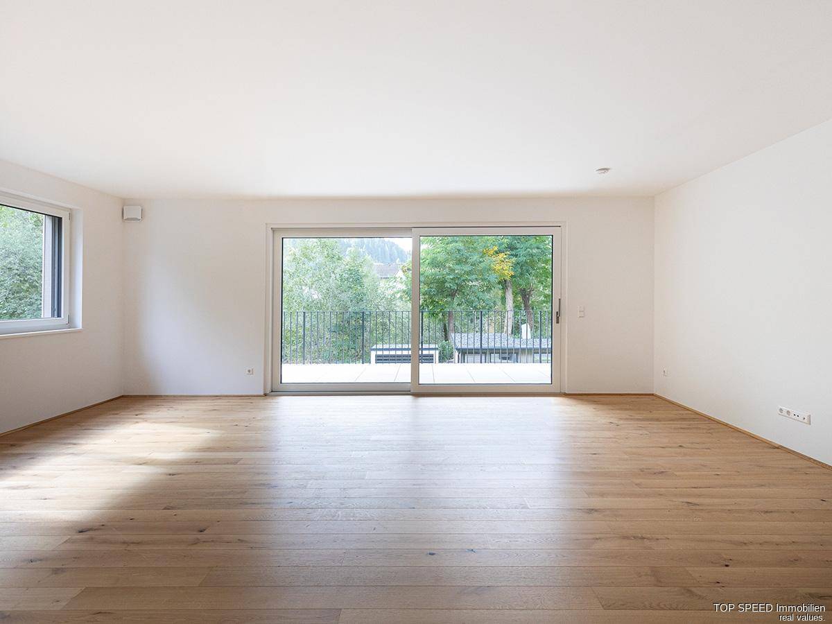 Lichtdurchfluteter Wohnbereich mit hellem Parkettboden und bodentiefen Fenstern zum Balkon.