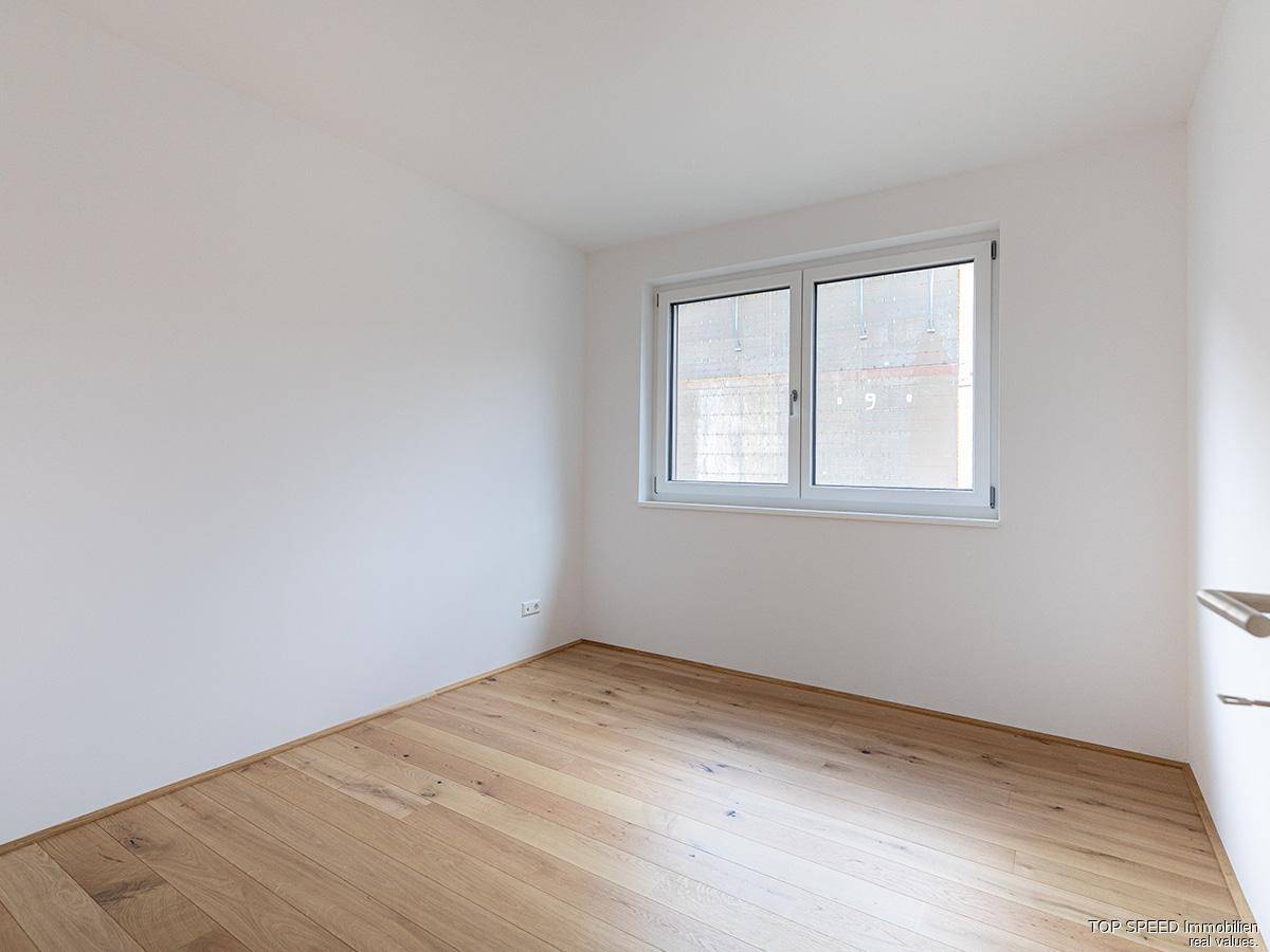Ruhiges Schlafzimmer mit hellem Parkettboden und einem Fenster für natürliche Belichtung.