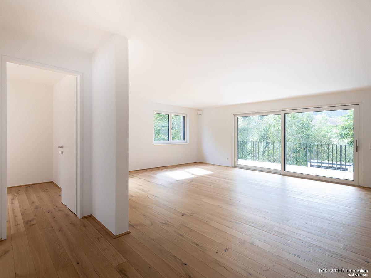 Helles, leeres Wohnzimmer mit Eichenparkettboden und Zugang zu einem großen Balkon.
