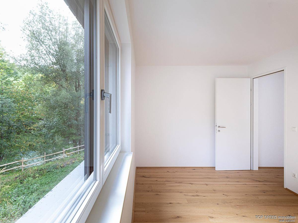 Helles Zimmer mit Parkettboden und großem Fenster mit Blick ins Grüne.