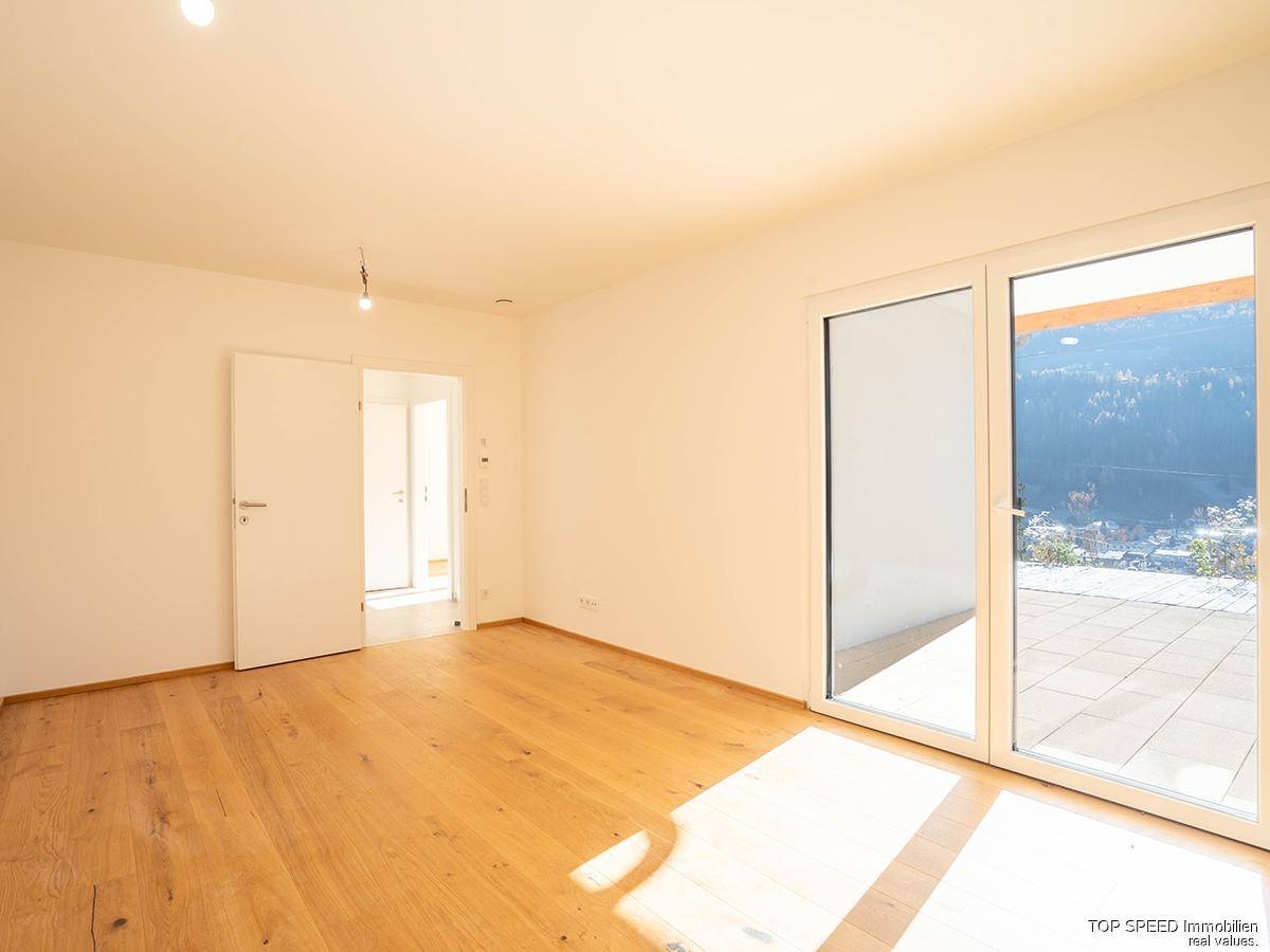 Heller, leerer Raum mit Holzboden und großen Glastüren, die auf eine Terrasse führen.