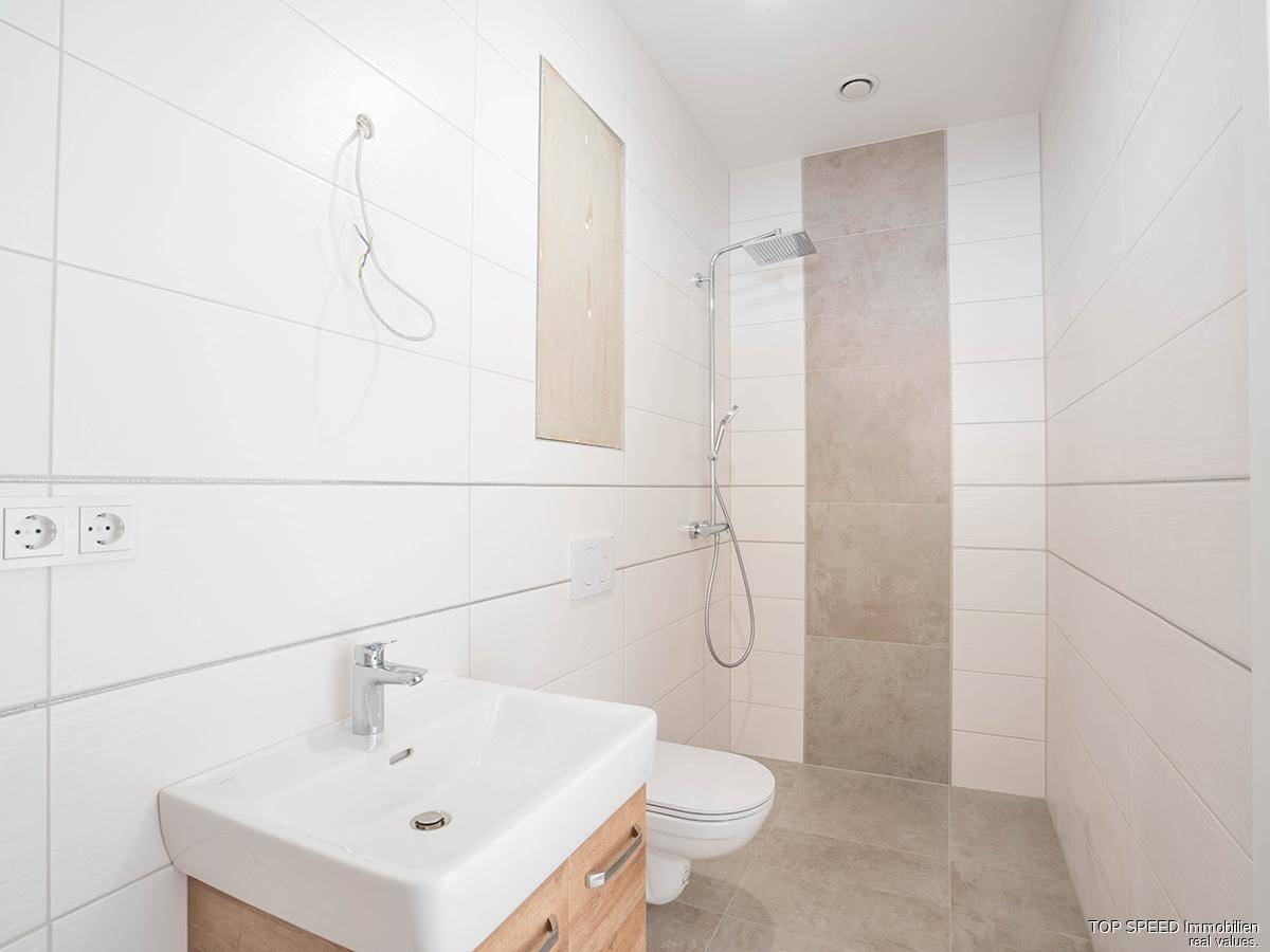 Modernes Badezimmer mit weißen Fliesen, Holzwaschtisch, Toilette und Regendusche.