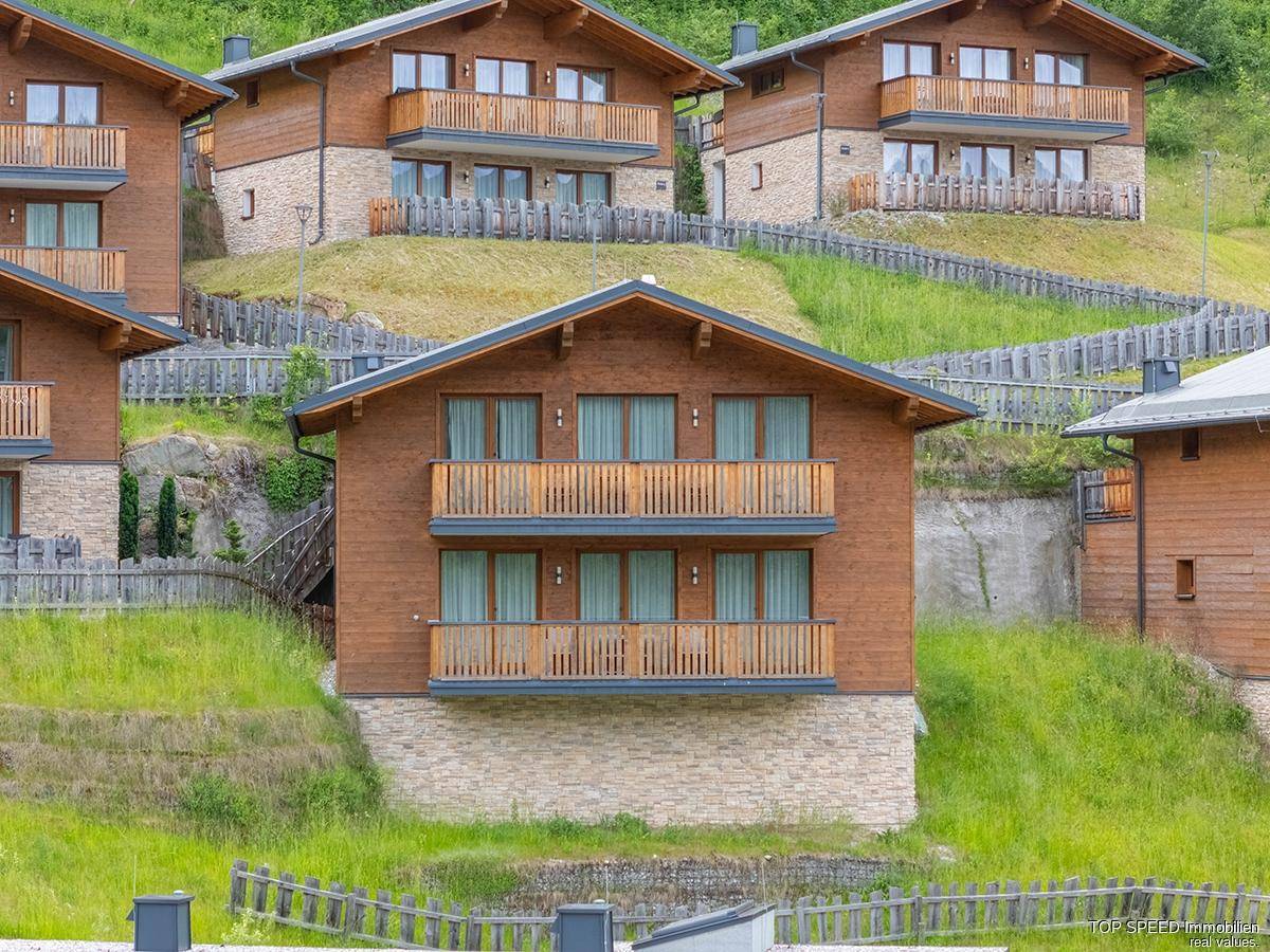 Nahaufnahme eines modernen Holzchalets mit mehreren Balkonen, eingebettet in eine grüne Hanglandschaft.