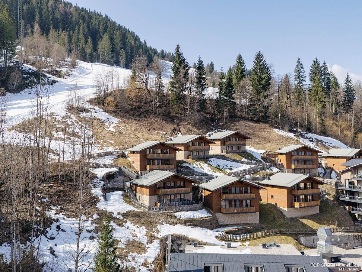 Winteransicht der Chaletanlage auf einem schneebedeckten Hang mit angrenzender Skipiste und Wald.