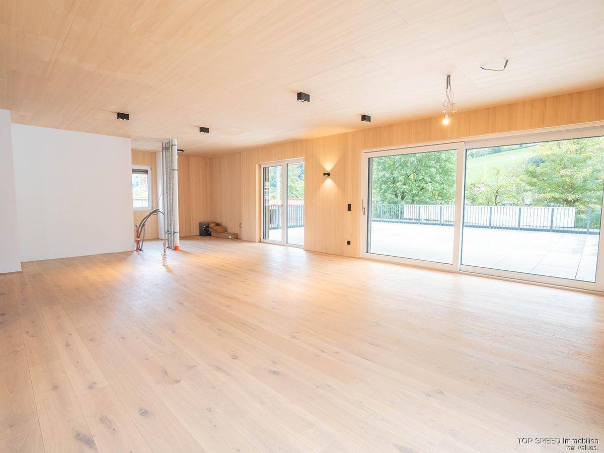 Geräumiger Wohnbereich mit Holzböden und großen Fensterfronten, die viel Tageslicht hereinlassen.