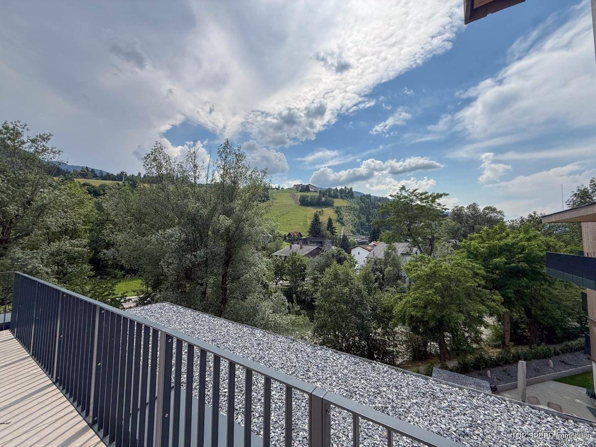 Weitblick über eine begrünte Landschaft und Dächer von einem Balkon oder einer Terrasse.