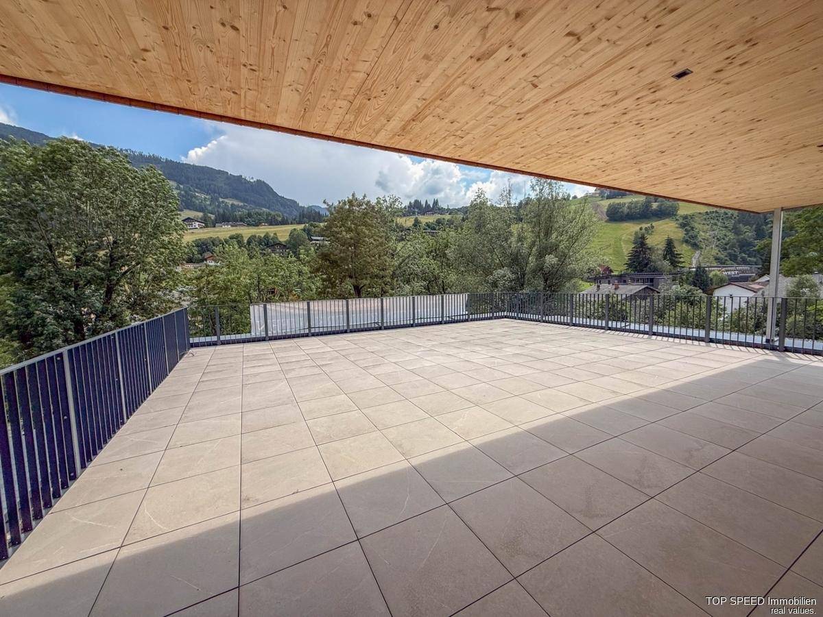 Große geflieste Terrasse mit Holzdecke und weitem Blick auf die umliegende grüne Hügellandschaft.