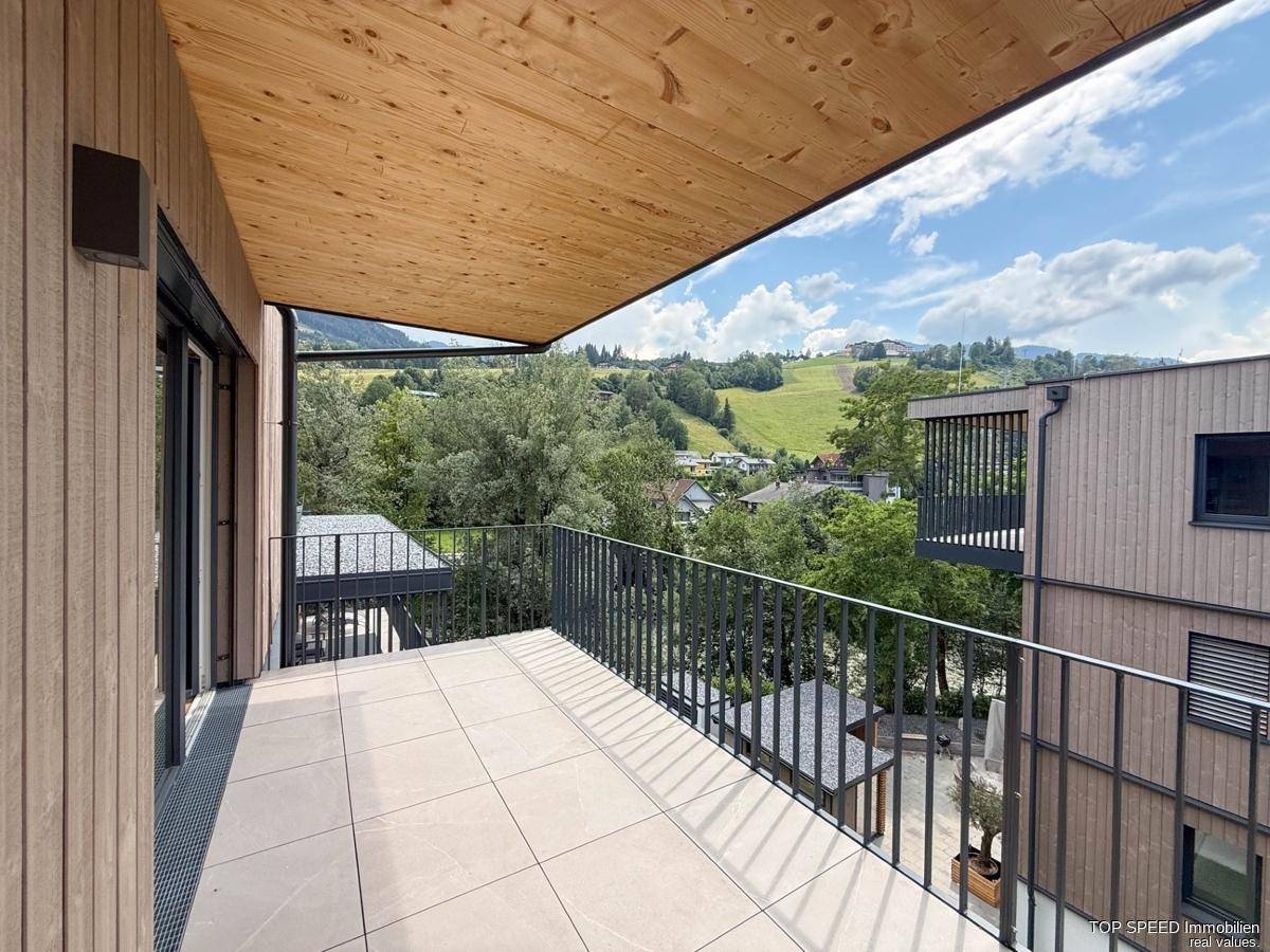 Moderner Balkon mit Fliesenboden und Holzverkleidung, bietet einen schönen Blick ins Grüne.