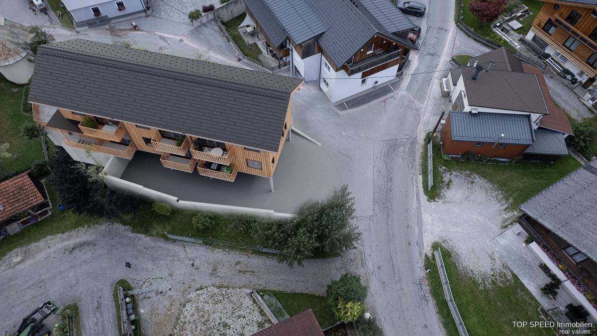 Luftaufnahme des modernen Holzgebäudes mit Balkonen und der umliegenden Bebauung in ländlicher Umgebung.