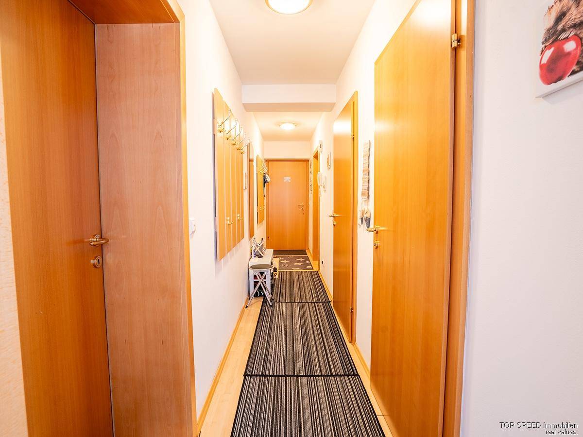 Heller Flur mit Holztüren, einem gestreiften Teppich und einer Garderobe.