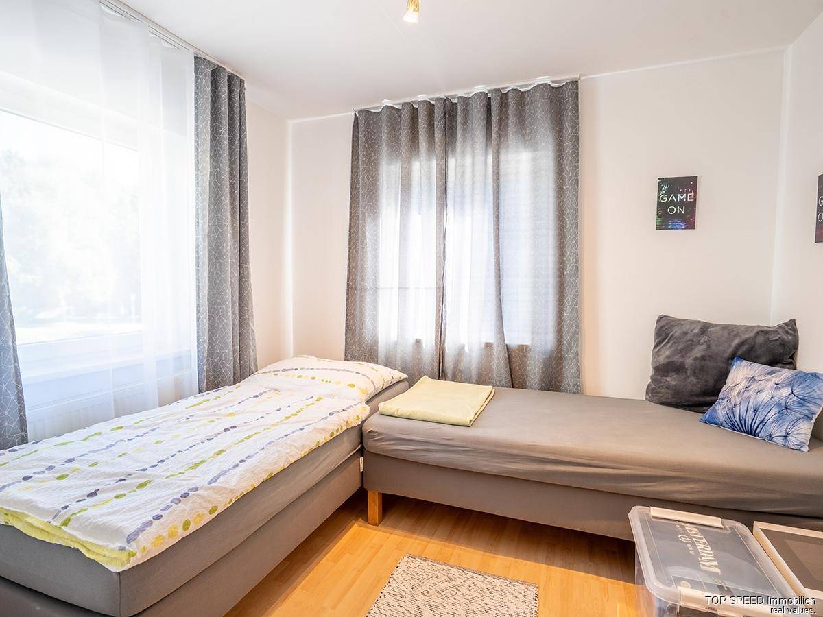 Freundliches Schlafzimmer mit zwei Einzelbetten, hellem Holzboden und einem großen Fenster.
