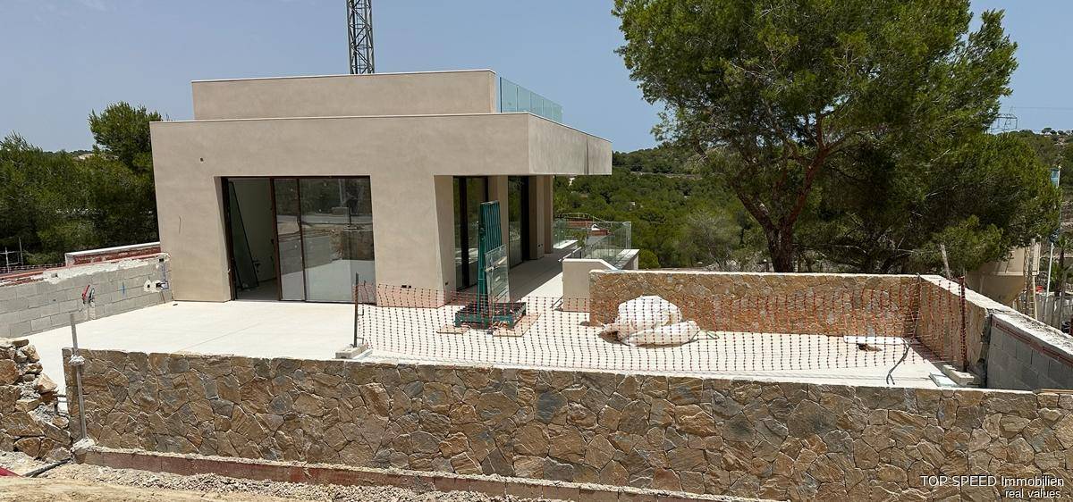 Baustelle einer modernen Villa mit Rohbau und vorbereiteter Terrasse, umgeben von Natur.