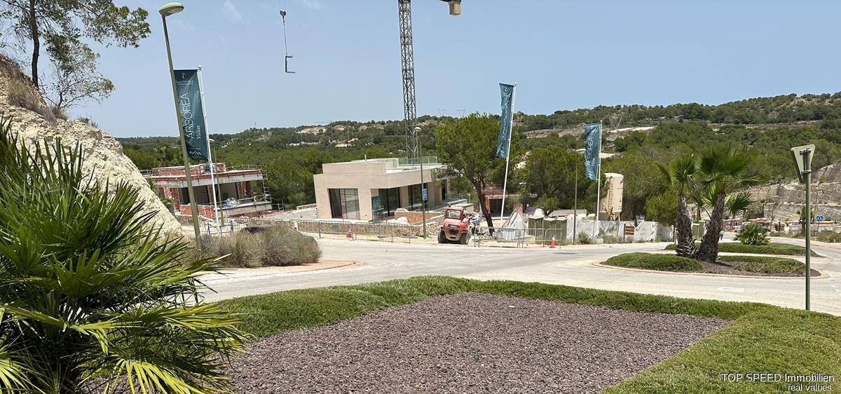 Baustelle einer modernen Villa in hügeliger Landschaft mit weiteren Gebäuden im Hintergrund.