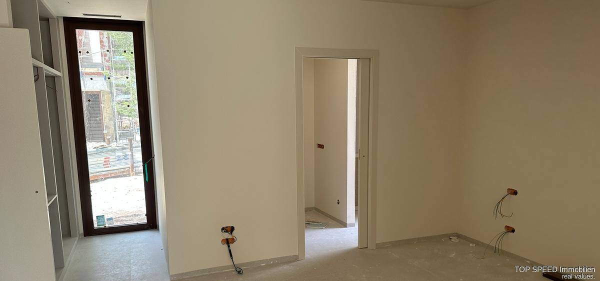 Innenraum im Rohbau mit Türrahmen und vorbereiteten Elektroinstallationen.