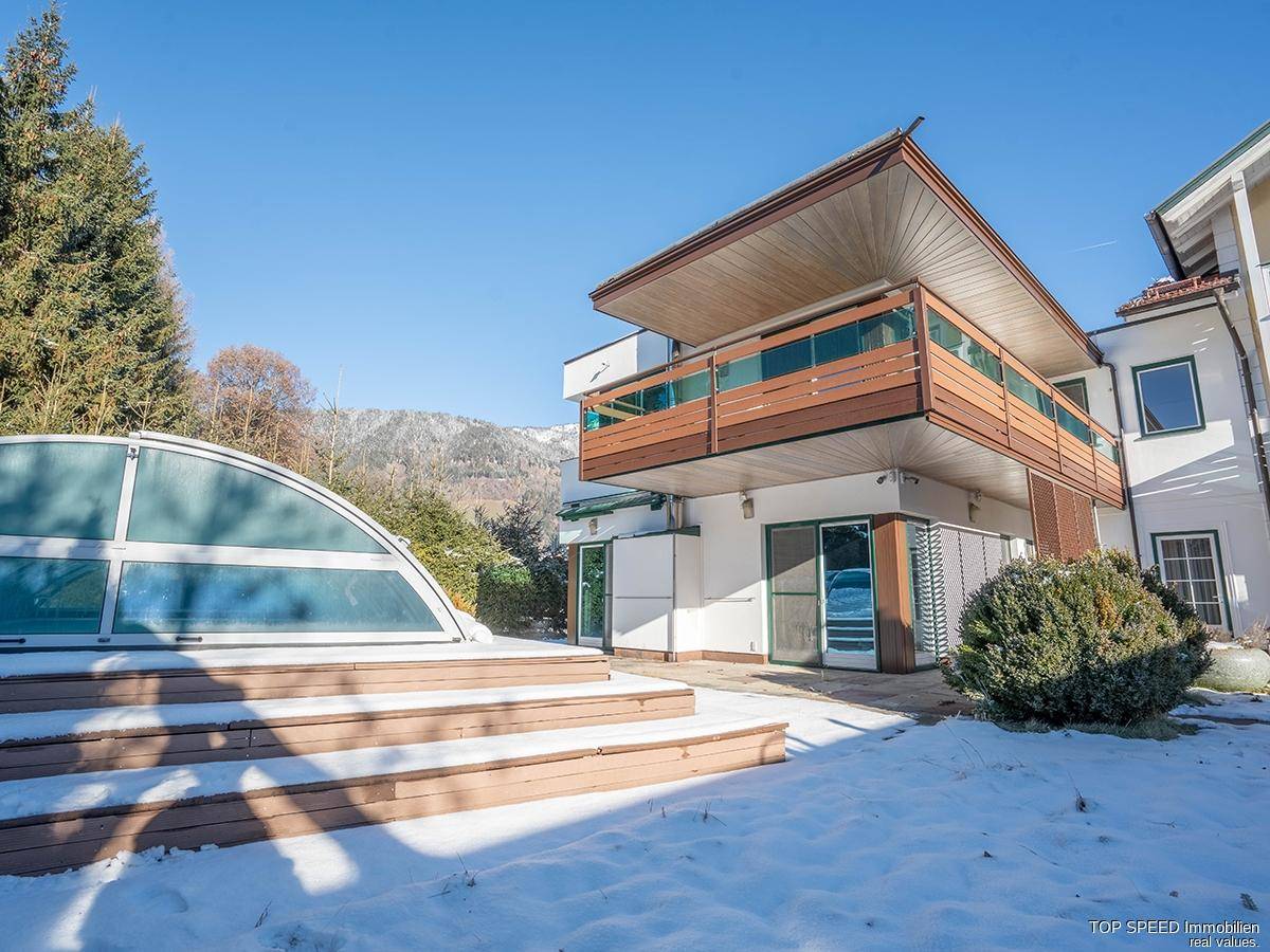 Modernes Gebäude mit Balkon und überdachtem Poolbereich im verschneiten Garten.