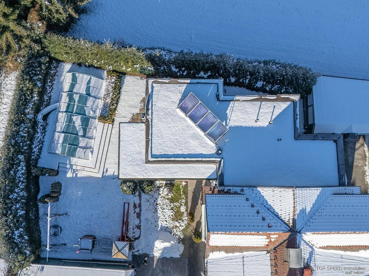 Vogelperspektive des Hauses mit Flachdach, Solaranlage und umgebender Winterlandschaft.