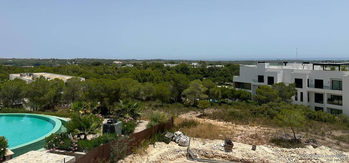 Weitläufiger Ausblick mit blauem Pool, grüner Landschaft und dem Meer am Horizont.