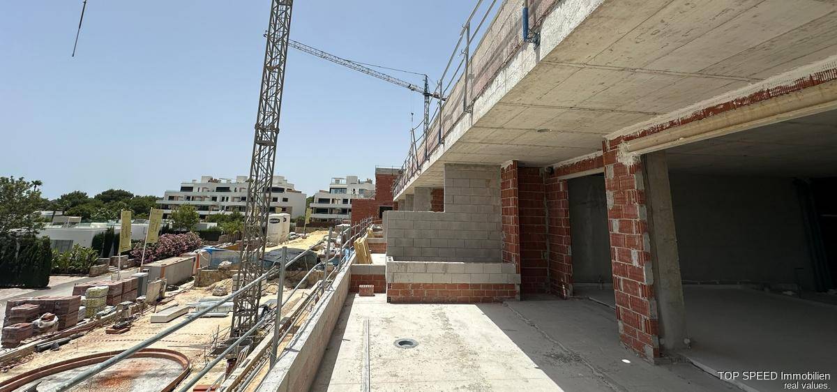 Blick von einem unfertigen Balkon auf die Baustelle mit weiteren Gebäuden und einem Kran.