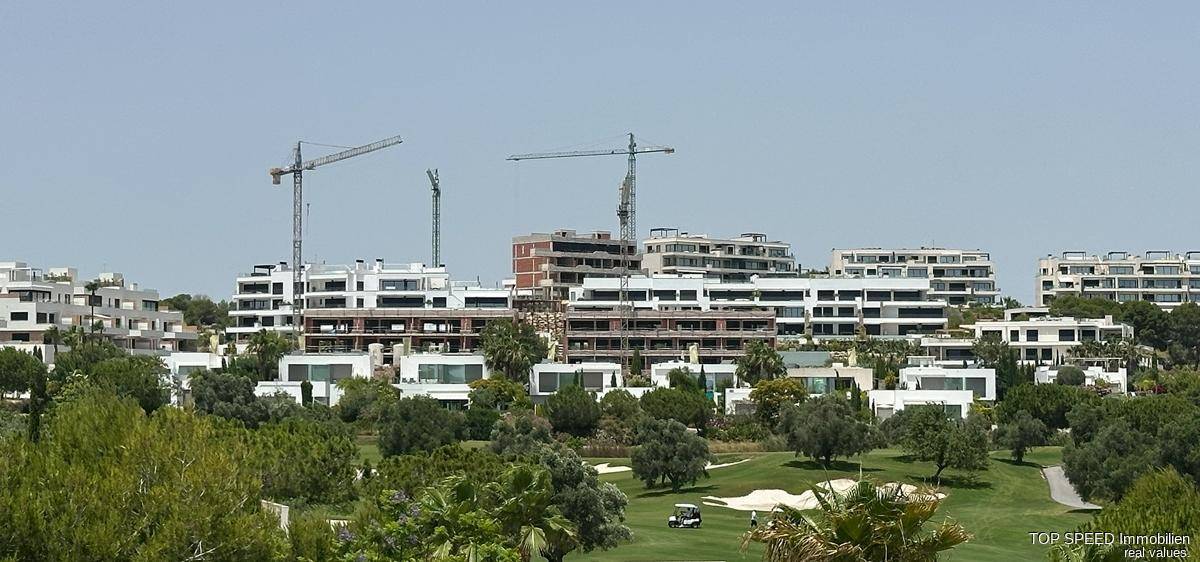 Panoramablick auf eine Wohnanlage im Bau mit Kränen und einem Golfplatz im Vordergrund.
