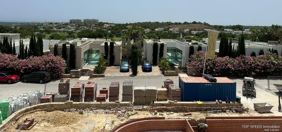Baustelle mit Poolfundament und Baumaterialien, umgeben von modernen Gebäuden und Vegetation.