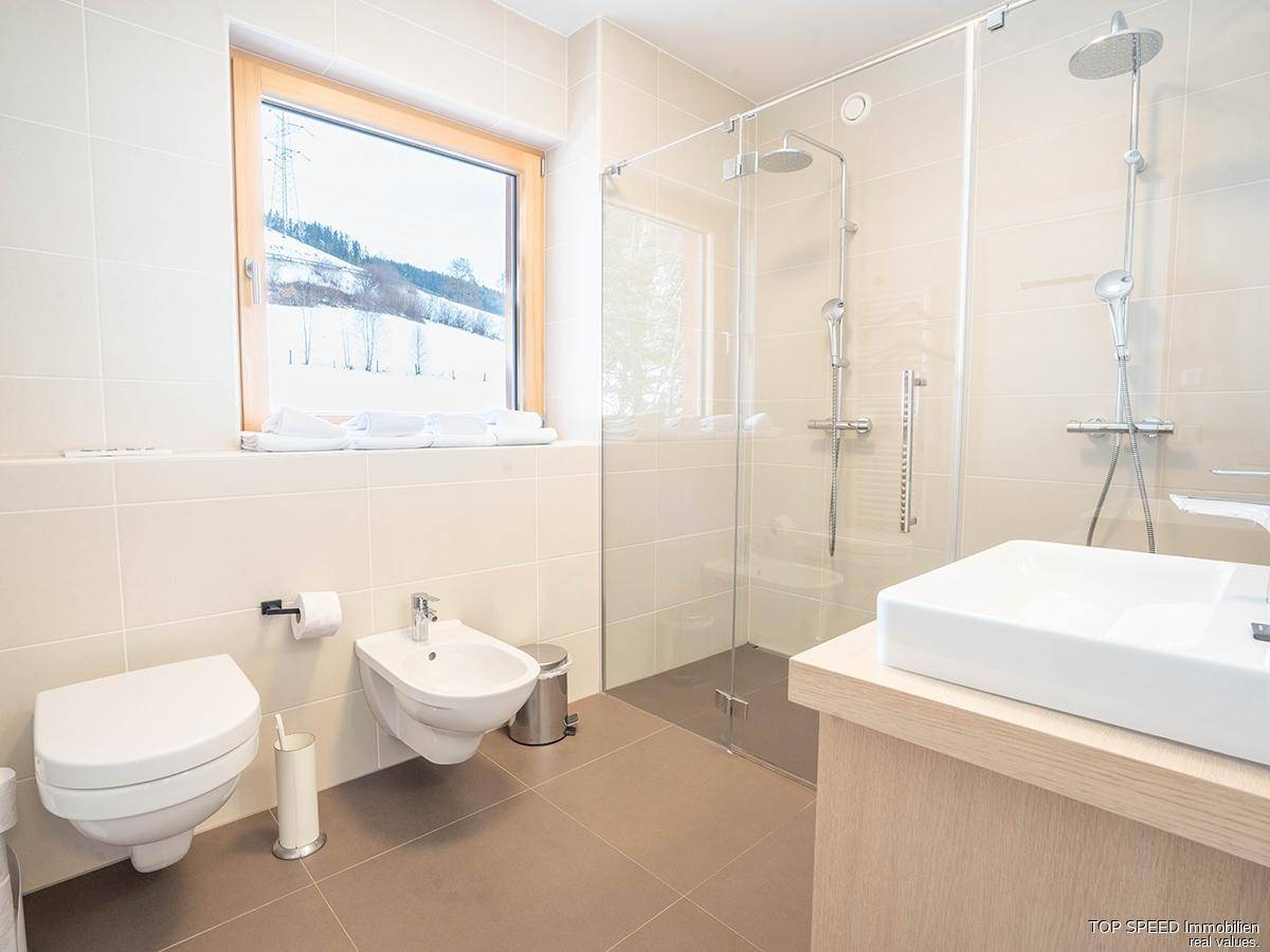 Modernes Badezimmer mit begehbarer Dusche, Bidet, WC und Fenster mit Blick auf die Winterlandschaft.