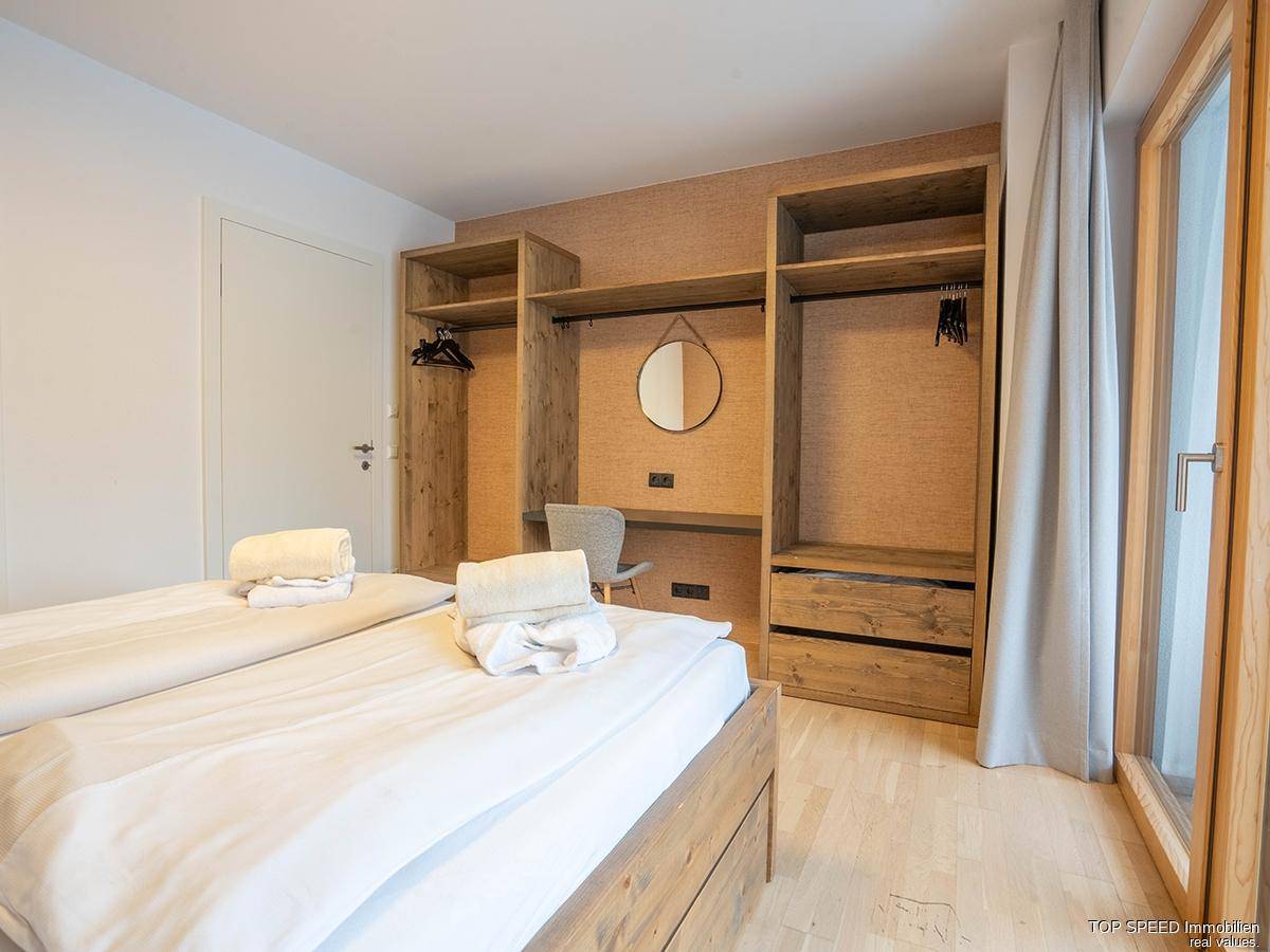 Schlafzimmer mit zwei Einzelbetten, offenem Holzschrank und einem Fenster für natürliches Licht.