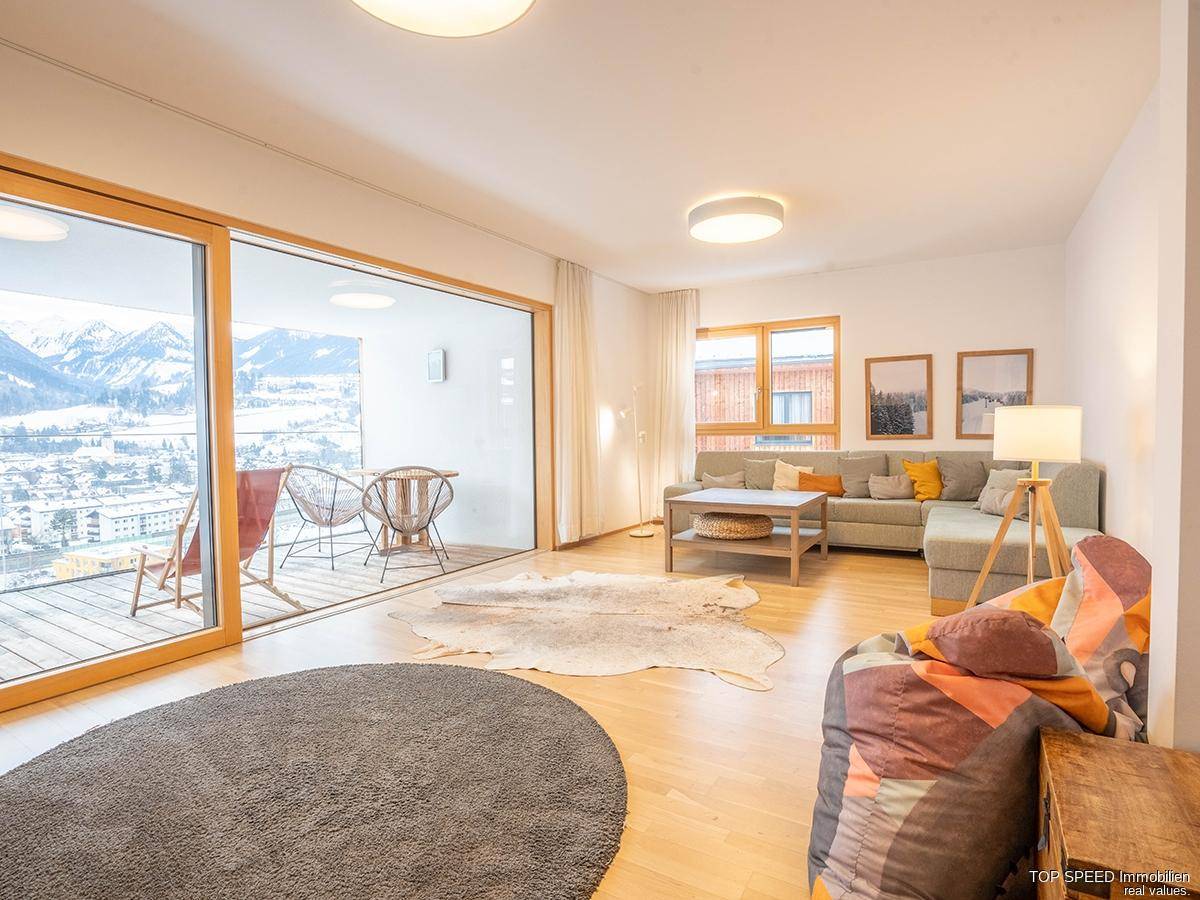 Helles Wohnzimmer mit modernem Sofa, Holzboden und großem Schiebefenster zum Balkon mit Bergblick.