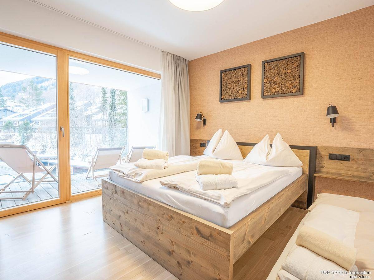 Gemütliches Schlafzimmer mit Holzbett, strukturierter Wand und Zugang zu einem Balkon mit Winterlandschaft.