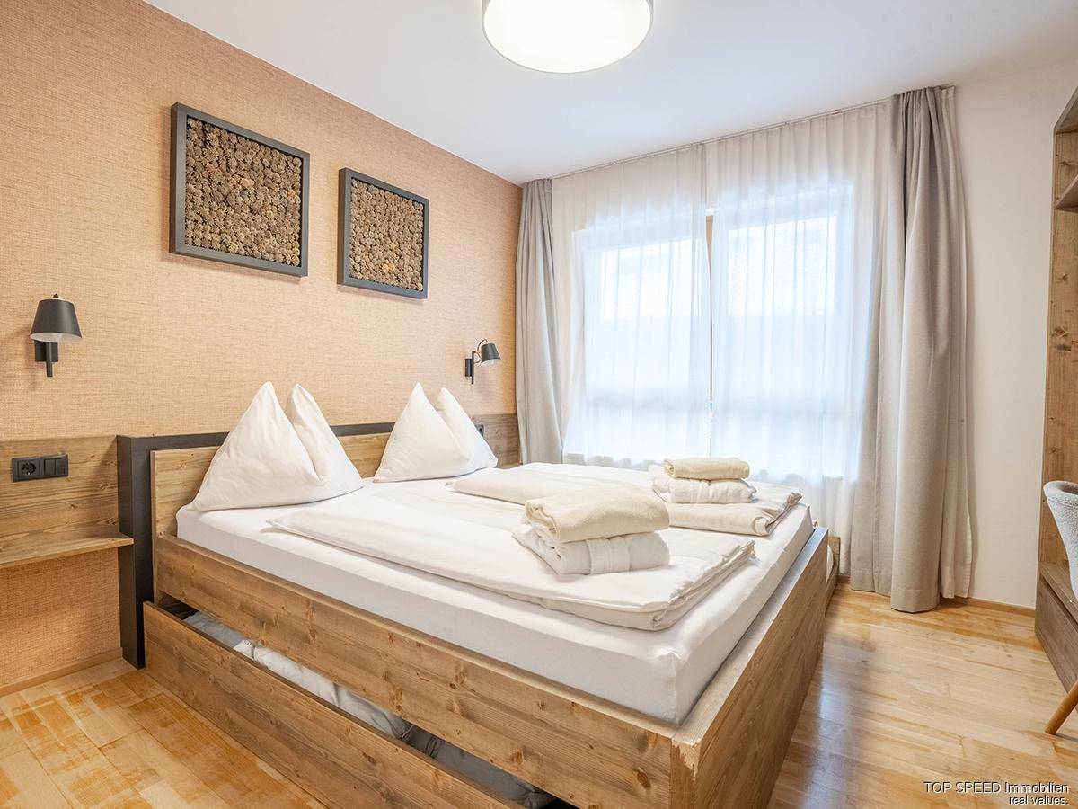 Helles Schlafzimmer mit Holzbett, dekorativer Wandgestaltung und großem Fenster für viel Tageslicht.