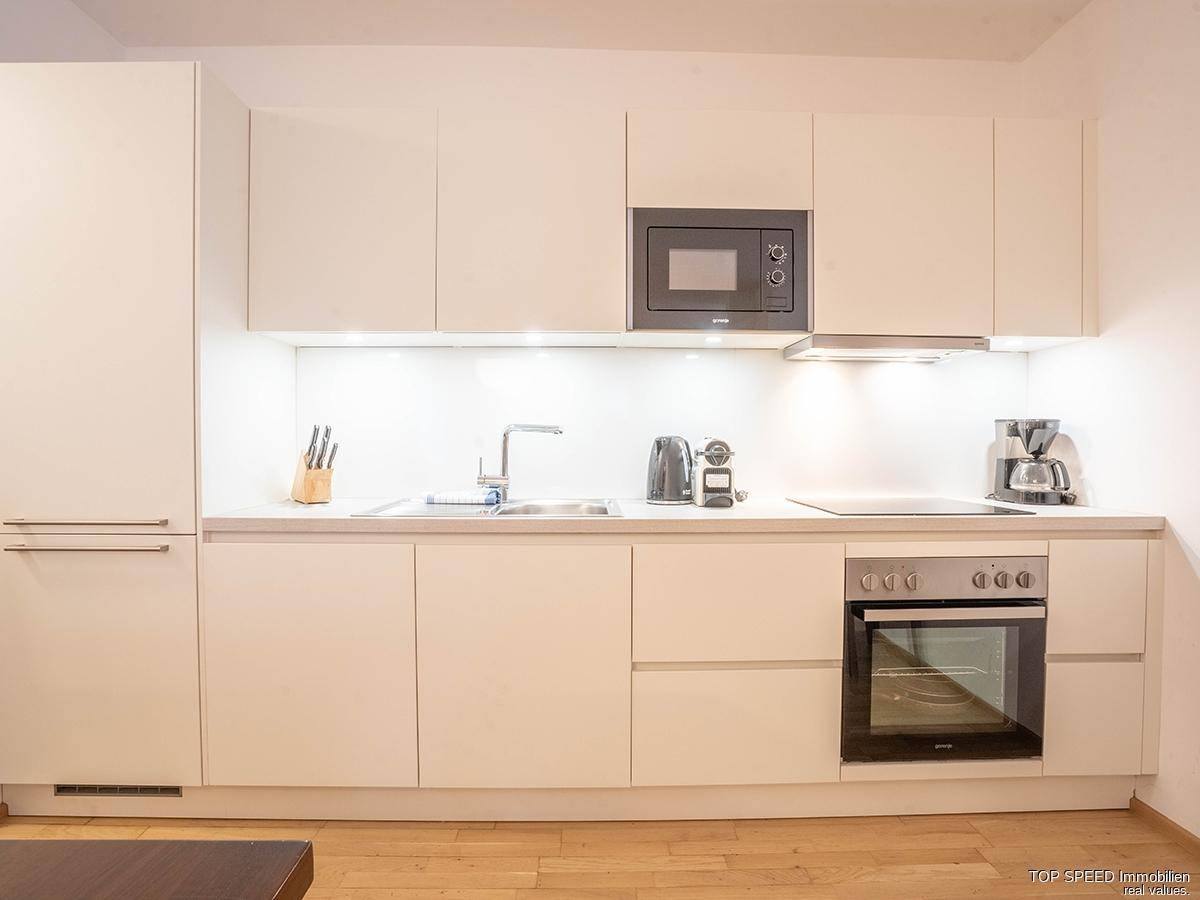 Moderne Einbauküche in Weiß mit integrierten Geräten wie Mikrowelle, Backofen und Induktionskochfeld.