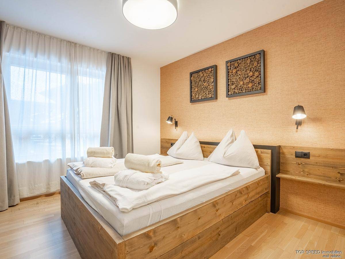 Gemütliches Schlafzimmer mit Holzbett, Wandleuchten und hellem Holzboden.