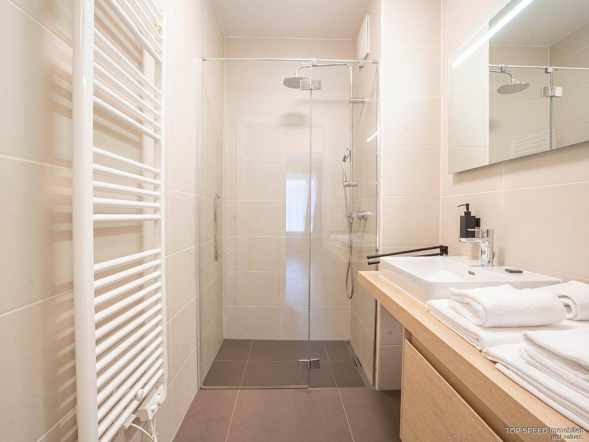 Modernes Badezimmer mit begehbarer Dusche, Einzelwaschbecken und beheiztem Handtuchhalter.