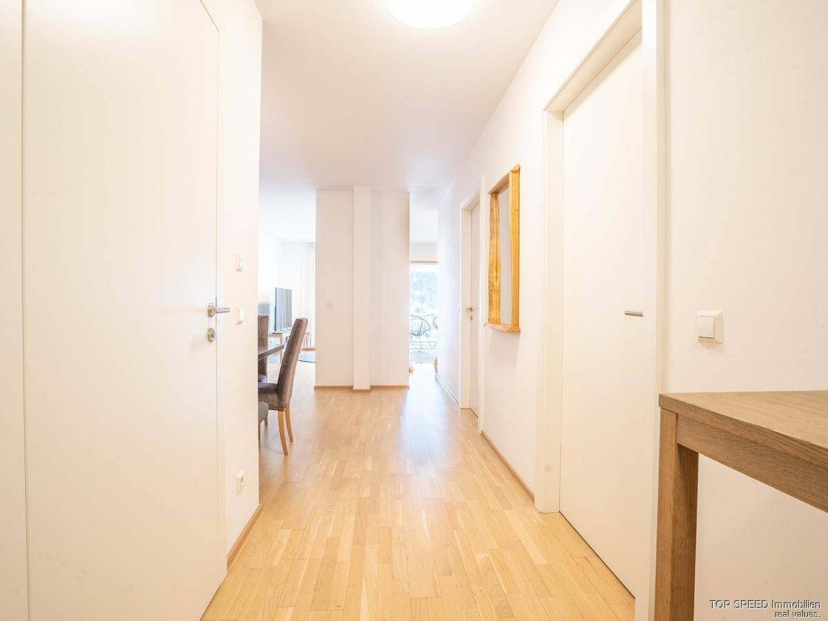 Heller Flur mit Holzboden und weißen Wänden, der zu den angrenzenden Wohnbereichen führt.