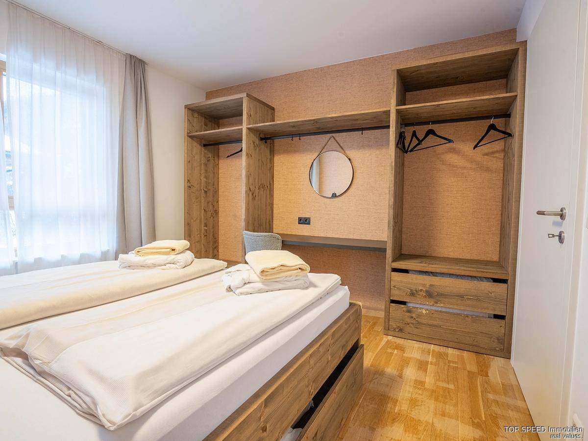 Schlafzimmer mit offenem Holzschrank, integriertem Schreibtisch und hellem Holzboden.