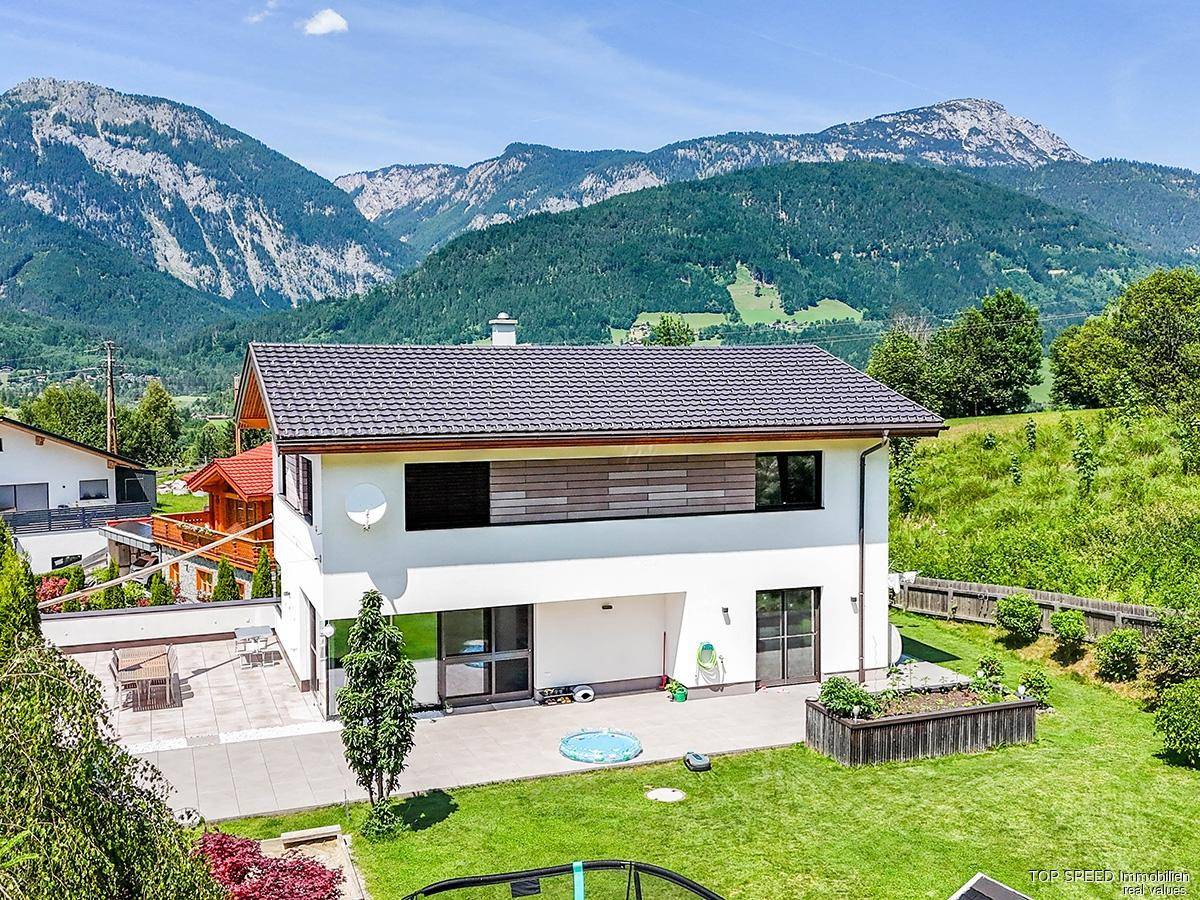 Rückseite des Hauses mit gepflegtem Garten, Terrasse und beeindruckendem Blick auf die Berge.