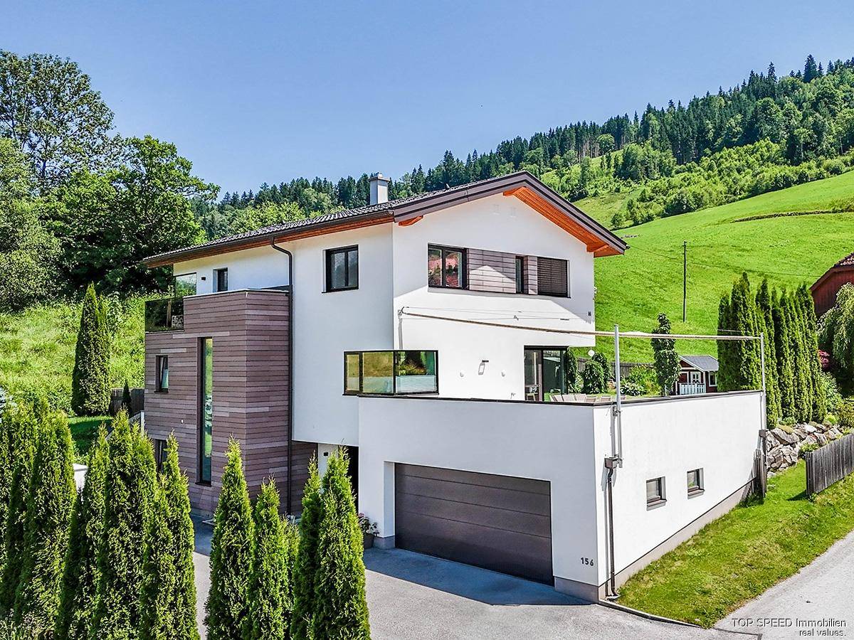 Ansicht des modernen Hauses von der Zufahrt, mit integrierter Garage und umliegender Naturlandschaft.