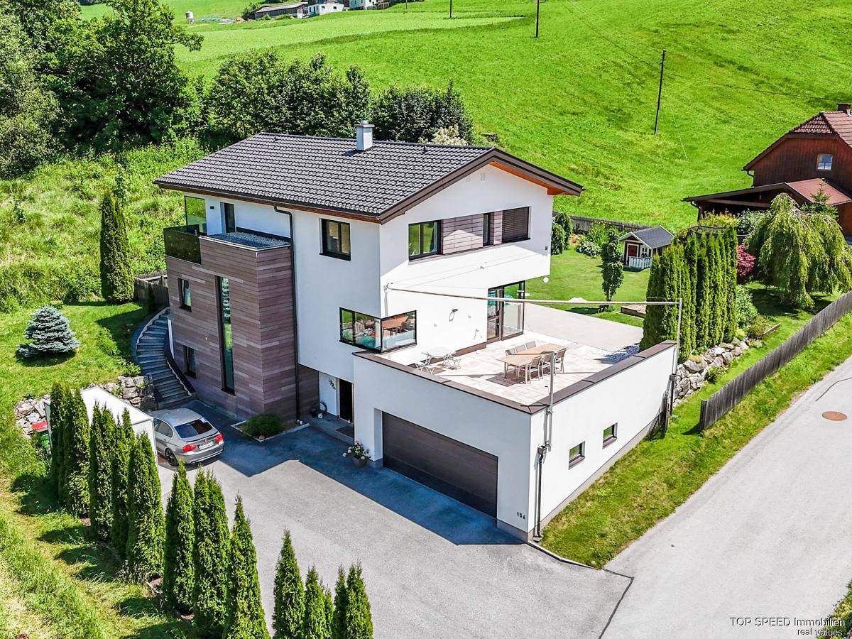 Modernes Haus mit großer Dachterrasse, Garage und Panoramablick auf die umliegende Berglandschaft.