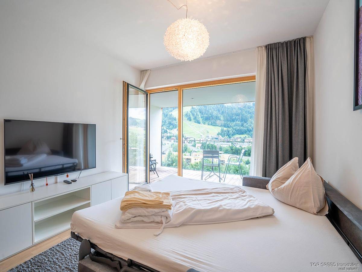 Gemütliches Schlafzimmer mit Bett, Fernseher und direktem Zugang zu einem Balkon mit Bergblick.