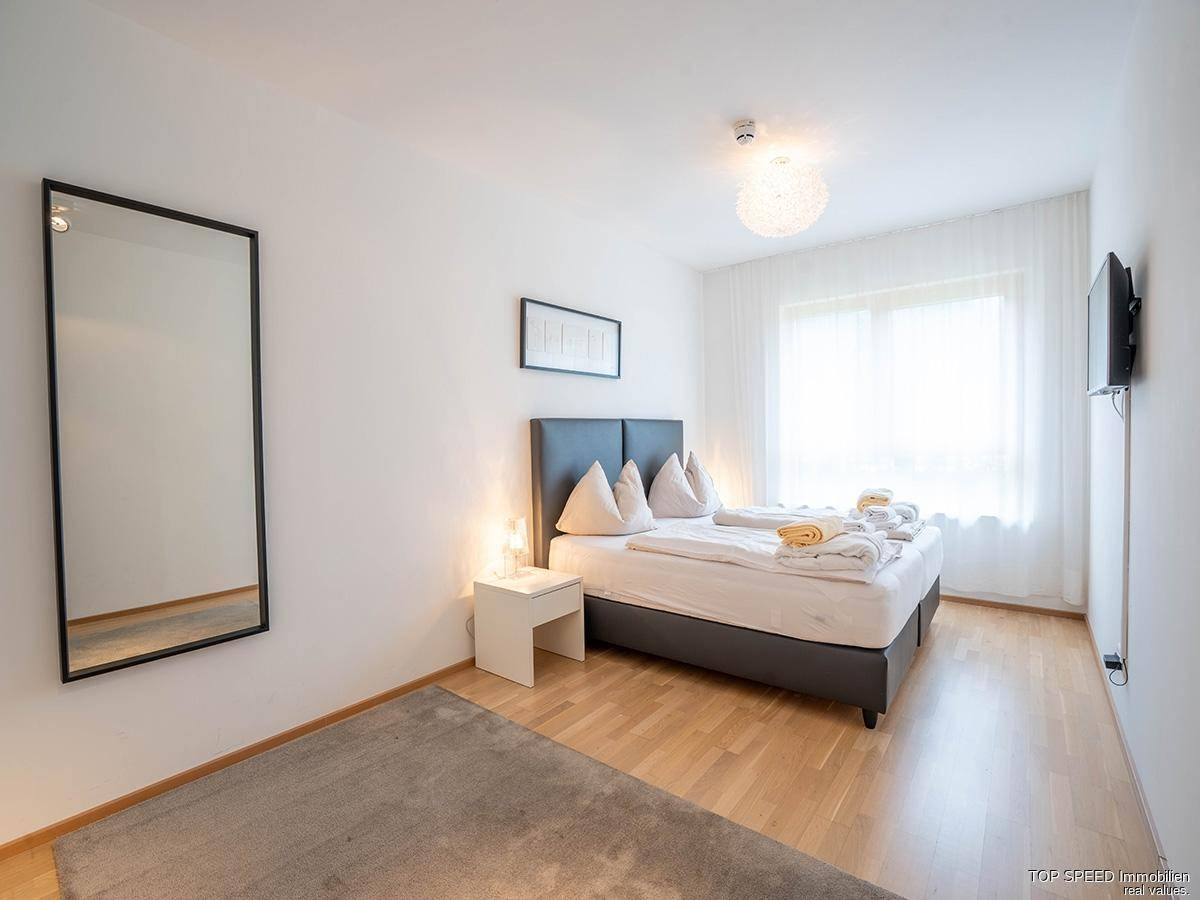 Helles Schlafzimmer mit Doppelbett, großem Spiegel und Fenster für viel Tageslicht.