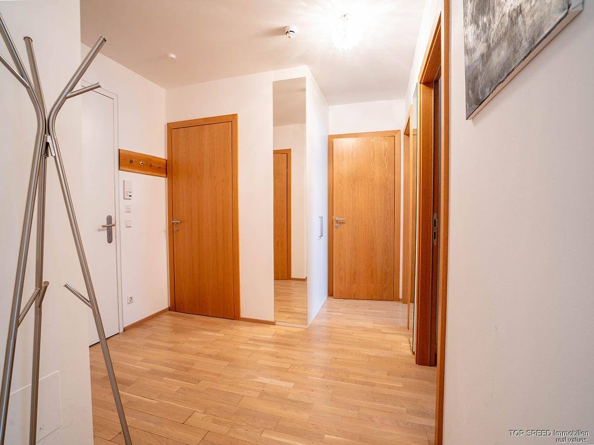 Heller Flur mit Holztüren, Parkettboden und einem Garderobenständer.