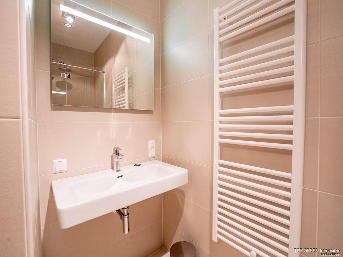 Badezimmer mit modernem Waschbecken, beleuchtetem Spiegel und beheiztem Handtuchhalter.