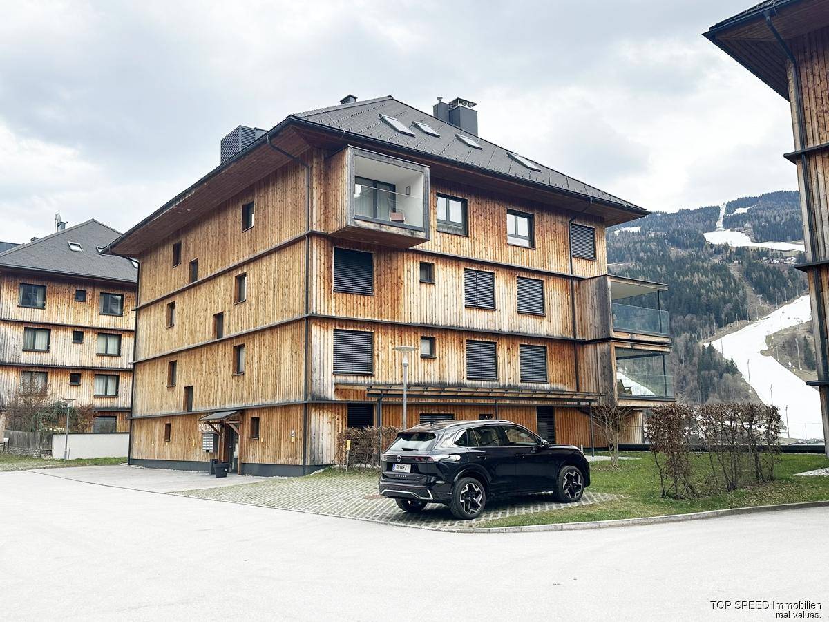 Modernes Gebäude mit Holzfassade, Balkonen und Blick auf die umliegende Berglandschaft.
